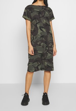 Olijfgroene camouflagejurk met korte mouwen, losse pasvorm en knielengte zoom. Gecombineerd met zwarte sneakers voor een casual uitstraling.