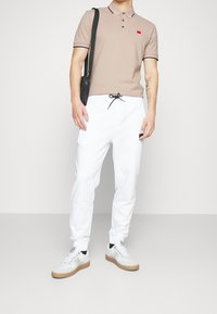 Polo beige avec deux boutons, col et manches noirs contrastants, pantalon blanc avec cordon de serrage, et baskets grises avec semelles en gomme.