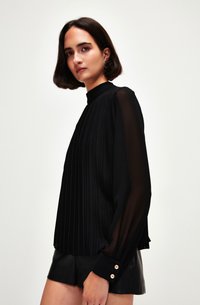 Blusa nera plissettata con colletto alto, maniche lunghe trasparenti e polsi con bottoni. Presenta una superficie testurizzata e una silhouette fluida.