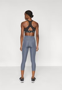 Μαύρο αθλητικό σουτιέν με σχέδιο racerback και διακοσμητική ταινία· γκρι κάπρι κολάν με λεία υφή και αντίθετες ραφές. Μαύρα αθλητικά παπούτσια.