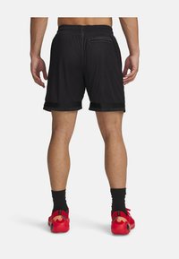 Shorts sportivi neri in rete con vita regolabile tramite cordino, caratterizzati da un orlo nero solido e dettagli rossi. Indossati con scarpe rosse e calze nere.