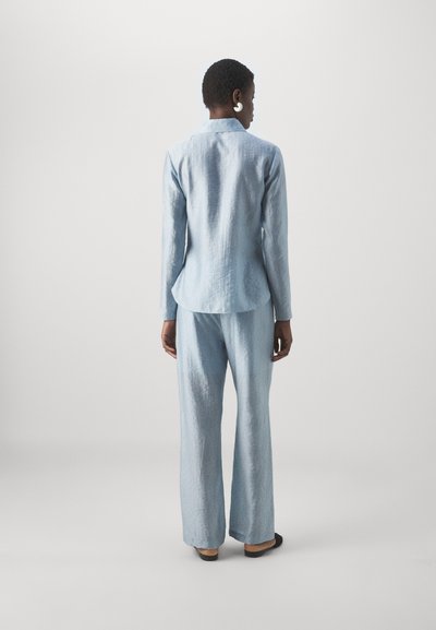 Ensemble deux pièces texturé bleu clair comprenant une chemise à manches longues avec col et un pantalon large, associé à des chaussures noires.