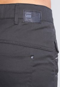 Ciemnoszare bawełniane spodnie z naszywką marki ze skóry, widocznym przeszyciem oraz bocznymi kieszeniami z metalowymi elementami.