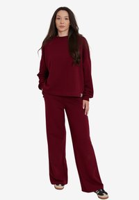 Burgundowy zestaw odzieży domowej składający się z luźnego swetra z długimi rękawami oraz pasujących spodni o szerokich nogawkach, wykonany z miękkiego, fakturowanego materiału.