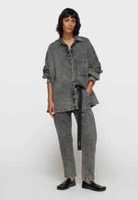 Camicia di denim grigia oversize con tasca, abbinata a pantaloni coordinati con un delicato motivo floreale. Scarpe nere flat completano l'outfit.