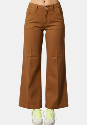 Pantaloni marroni a vita alta e gamba larga indossati con sneakers bianche con lacci giallo acceso.