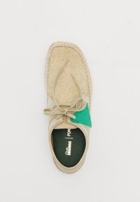 Beige suède schoen met een gestructureerde afwerking, groene tag, ronde neus en vetersluiting. Inclusief een zachte binnenzool met merknaamdetails.