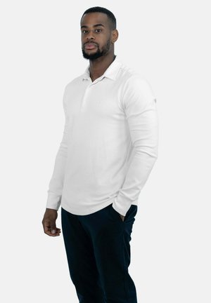Witte lange mouw polo shirt met een knoopsluiting, gemaakt van een gladde stof. De drager combineert het met donkerblauwe broeken.
