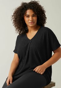 Schwarzes V-Ausschnitt-T-Shirt aus einem strukturierten Stoff mit einem zerknitterten Muster. Die Ärmel sind kurz und die Passform ist locker für maximalen Komfort.