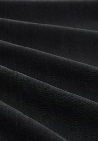 Tela negra con una textura suave, que presenta pliegues diagonales creando una apariencia en capas. El material es opaco con un ligero brillo.