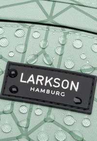 Tessuto verde menta texture con un motivo geometrico, gocce d'acqua visibili, con un'etichetta nera che riporta la scritta "LARKSON HAMBURG."