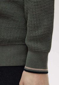 Maglione lavorato a maglia verde con texture e polsini a coste, caratterizzato da una base nera e una striscia di accentuazione rosa sull'orlo.