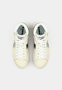 High-top sneakers in cream leather with black accents, featuring white laces, a padded collar, and a logo on the tongue.