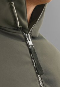 Felpa verde con zip metallico e tira in tessuto, texture liscia e cappuccio aderente tagliato corto.