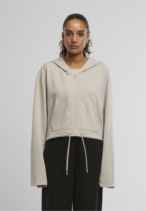 Beskåret beige hættetrøje med lynlås foran, store forlommer, snoretræk ved kanten og en afslappet pasform. Blød, glat tekstur med lange ærmer.