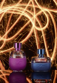 Bouteilles de parfum Hollister Festival Nite : une violette avec une finition mate texturée et une autre bleu foncé, toutes deux avec des bouchons transparents et des logos de la marque.