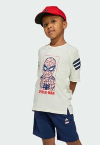 Biela tričká s krátkym rukávom so grafikou Spiderman a červeným nápisom. Námornícke šortky s bielymi pruhmi. Červená čiapka s čiernym šiltom.