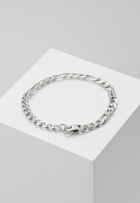 Pulsera de cadena de plata con eslabones entrelazados y cierre de gancho, exhibida en un pedestal minimalista blanco.