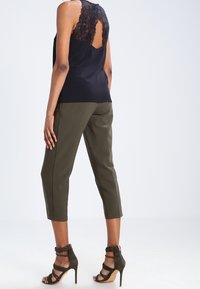 Czarna satynowa bluzka z koronkowymi detalami z tyłu, zestawiona z oliwkowymi spodniami 3/4 i ciemnozielonymi sandałami na obcasie.