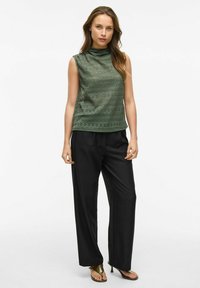 Groene kanten mouwloze top met hoge hals gecombineerd met zwarte wijde broek. De outfit heeft een gestructureerd design en een ontspannen pasvorm.