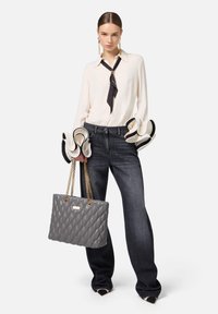 Borsa grigia trapuntata con manici a catena dorati, camicia crema con cravatta nera e jeans scuri a gamba larga. Note distintive delle maniche con polsini svasati.