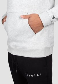 Light gray sweatshirt with a front pocket and ribbed cuffs. Black drawstring sweatpants feature white "NOROTAI" logo on the leg.