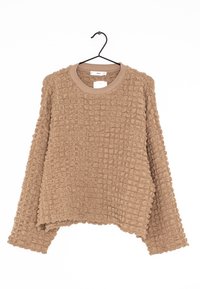 Pull beige texturé oversize avec col rond, présentant un motif gaufré et des manches larges, suspendu à un crochet noir.