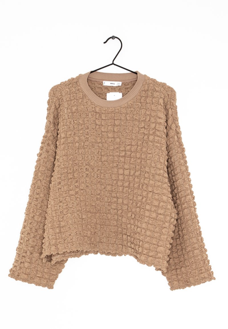 Pull beige texturé oversize avec col rond, présentant un motif gaufré et des manches larges, suspendu à un crochet noir.