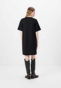 Černé oversized tričko šaty s krátkými rukávy, hladká látka, ke kolenům, nošeno s černými kozačkami po kolena s akcentem zlatého řetězu.