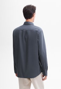 Maglietta a manica lunga grigia con colletto classico, polsini abbottonati e orlo dritto. Realizzata in tessuto liscio con una sottile texture.