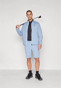 Φωτεινό γαλάζιο γκολφ μπουφάν, μαύρο πόλο και ταιριαστά σορτς· το μοντέλο κρατάει ένα γκολφ ρόπαλο· μαύρα παπούτσια και κάλτσες· λείο ύφασμα· casual σχεδιασμός.