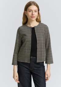 Veste à motifs noir et blanc avec un col rond, des manches trois-quarts et une coupe droite, associée à un jean foncé.