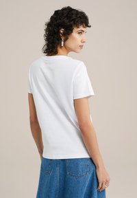 Balta trumpų rankovių marškinėliai, pagaminti iš minkštos medvilnės, su įprasta pritaikymo forma. Stilingi su apvalia iškirpte, matomi iš nugaros.