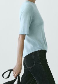 Maglione a maniche corte in maglia azzurro chiaro con polsini e orlo a coste, abbinato a jeans in denim nero. La texture appare morbida e leggera.