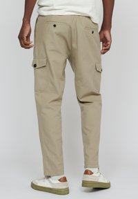 Beige Cargo-Hosen mit schmalem Schnitt, ausgestattet mit zwei Seitentaschen und zwei Gesäßtaschen, aus strukturiertem Stoff. Tragen mit weißen Sneakers.