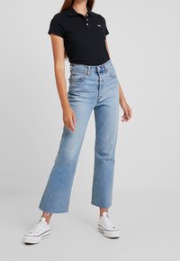 Svart polo t-shirt med tvåknappsstängning, kombinerad med ljusblå högmidjade jeans och vita kanvas sneakers.