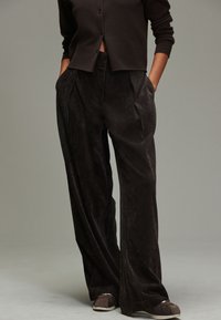 Spodnie sztruksowe w ciemnobrązowym kolorze, o szerokich nogawkach, z zakładkami z przodu i bocznymi kieszeniami. Połączone z ciemnym kardiganem na guziki.