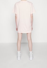 Světle růžové bavlněné tričko s volným střihem, krátkými rukávy a kulatým výstřihem, nošené s bílými teniskami a bílými podkolenkami.