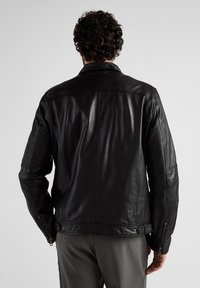 Schwarze Lederjacke mit matter Oberfläche, die ein maßgeschneidertes Design, Reißverschlüsse an den Ärmelbündchen und subtile Nähdetails auf dem Rücken aufweist.