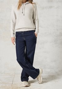 Světlý béžový žebrovaný svetr s kapucí na stahovací šňůrku, kombinovaný s tmavě modrými širokými džíny s kontrastním prošitím a předními kapsami.