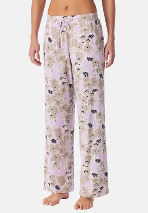 Femme portant un pantalon de pyjama ample lavande avec un motif floral beige et noir et une taille à cordon, debout pieds nus.