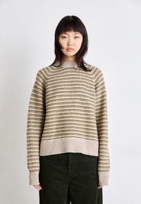 Beige- und gelb gestreifter Pullover mit gerippten Bündchen und Saum, mit lässigem Schnitt und weicher Textur, getragen mit dunkelgrünen Cordhosen.
