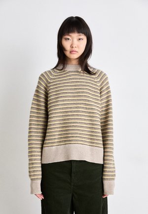 Beige and yellow striped sweater with ribbed cuffs and hem, featuring a relaxed fit and soft texture, worn with dark green corduroy pants.
