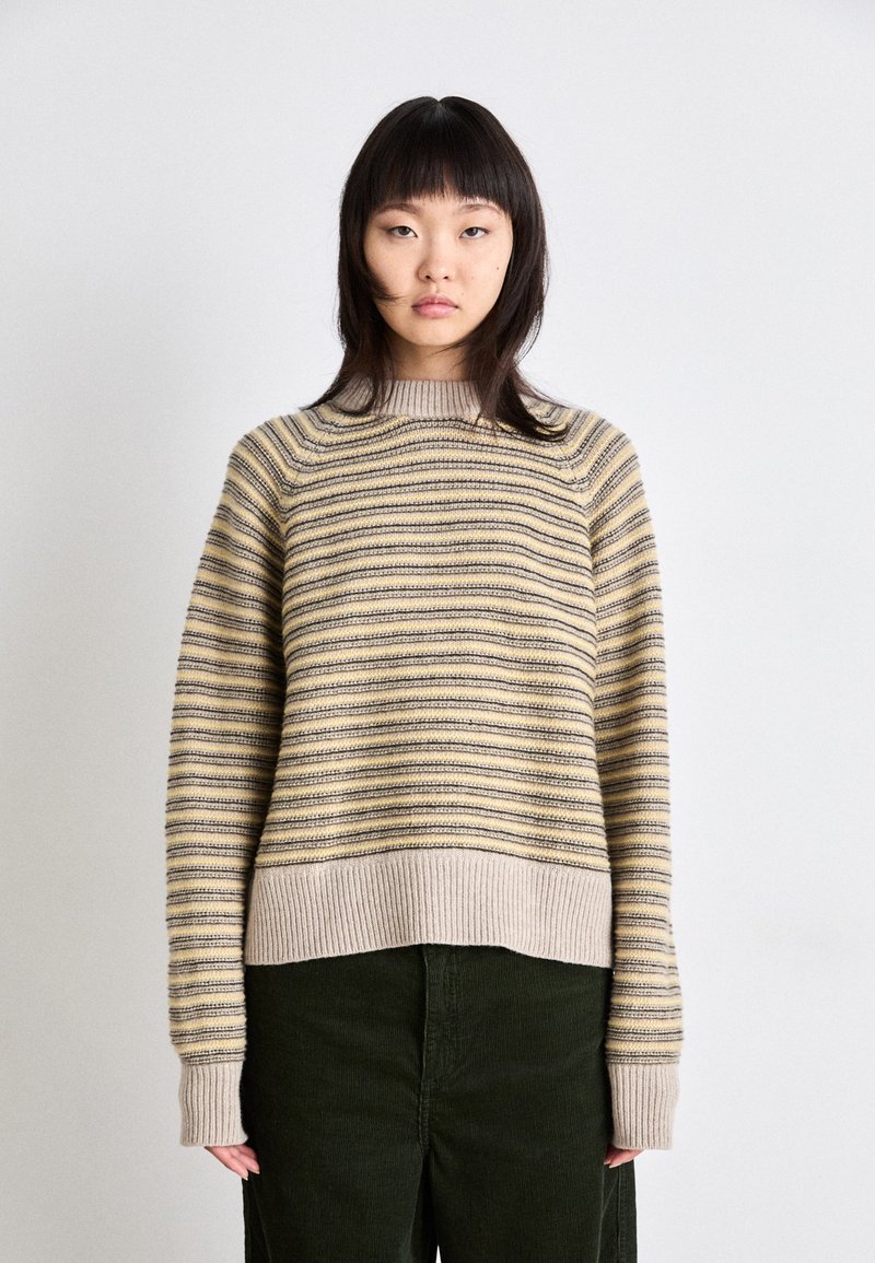 Beige- und gelb gestreifter Pullover mit gerippten Bündchen und Saum, mit lässigem Schnitt und weicher Textur, getragen mit dunkelgrünen Cordhosen.