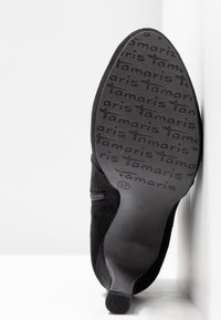 Semelle de chaussure à talon noir avec motif du logo « Tamaris », taille 37, vue par le dessous avec une fermeture éclair visible sur le côté.
