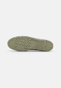 Semelle de chaussure en caoutchouc avec un motif texturé comportant des formes de diamants et géométriques. Principalement verte avec des éclats multicolores à travers.