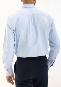 Lichtblauw overhemden met lange mouwen, achterpand en verstelbare manchetten, gecombineerd met donkerblauwe broek met een achterzak.
