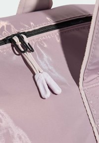 Ανοιχτό μωβ τσάντα με γυαλιστερό, υφασμάτινο ανάγλυφο ύφασμα. Μαύρο φερμουάρ με διπλούς μηχανισμούς έλξης· οι μηχανισμοί έχουν λευκές πλαστικές άκρες. Κοντινή λήψη, που τονίζει  τις λεπτομέρειες.