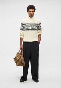 Camisola de gola alta em malha cremosa com padrões geométricos em preto e azul, combinada com calças largas pretas e uma mala de couro castanha.