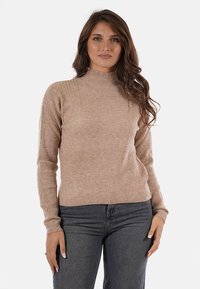 Maglione a collo alto a coste in beige chiaro, con maniche lunghe e delicate cuciture decorative lungo le spalle. Texture morbida.